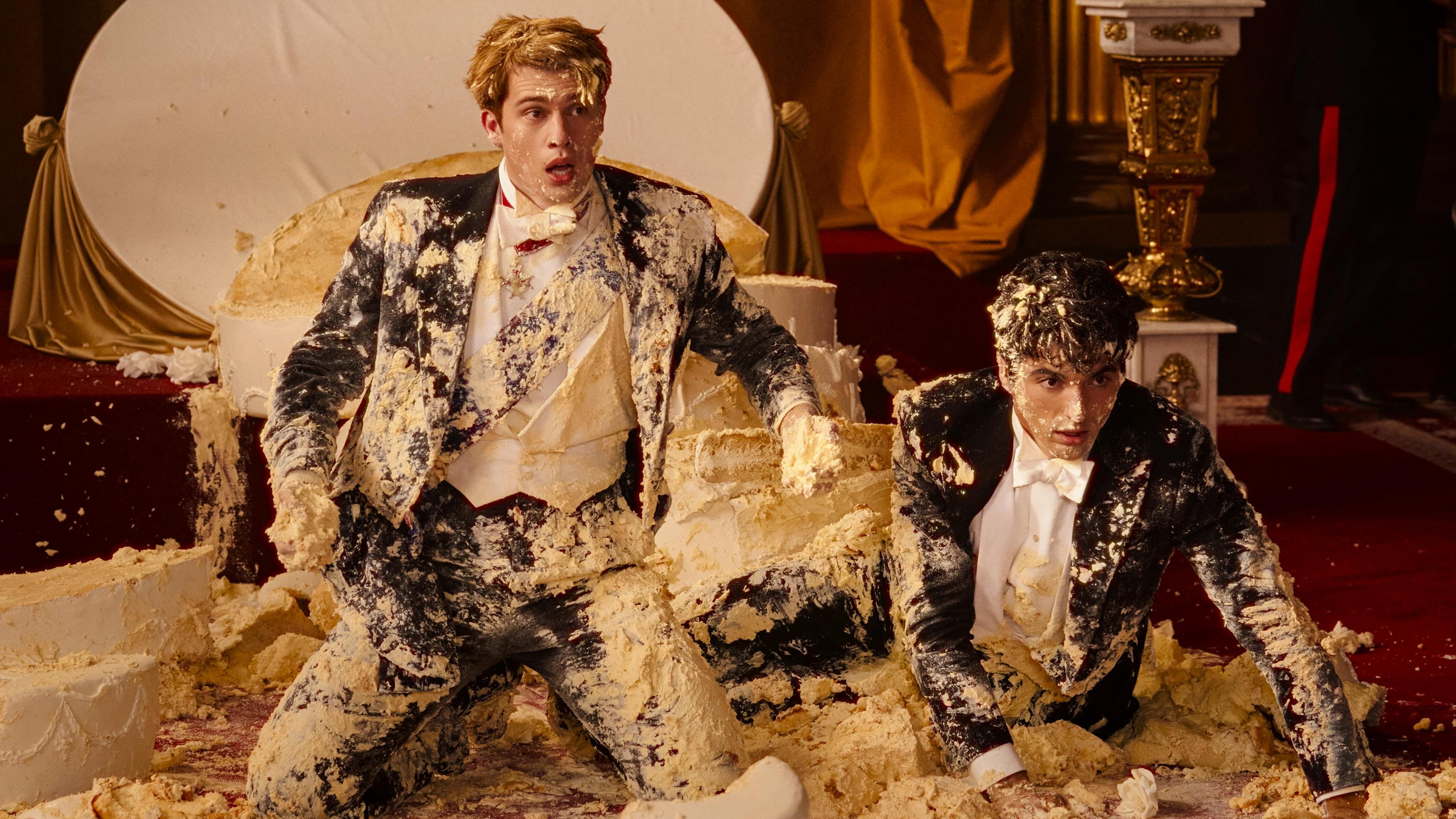 Red, White &amp; Royal Blue still: Alex (Perez) and Prince Henry (Galitzine) on the floor covered in cake and icing after a royal tower cake collapsed on them.