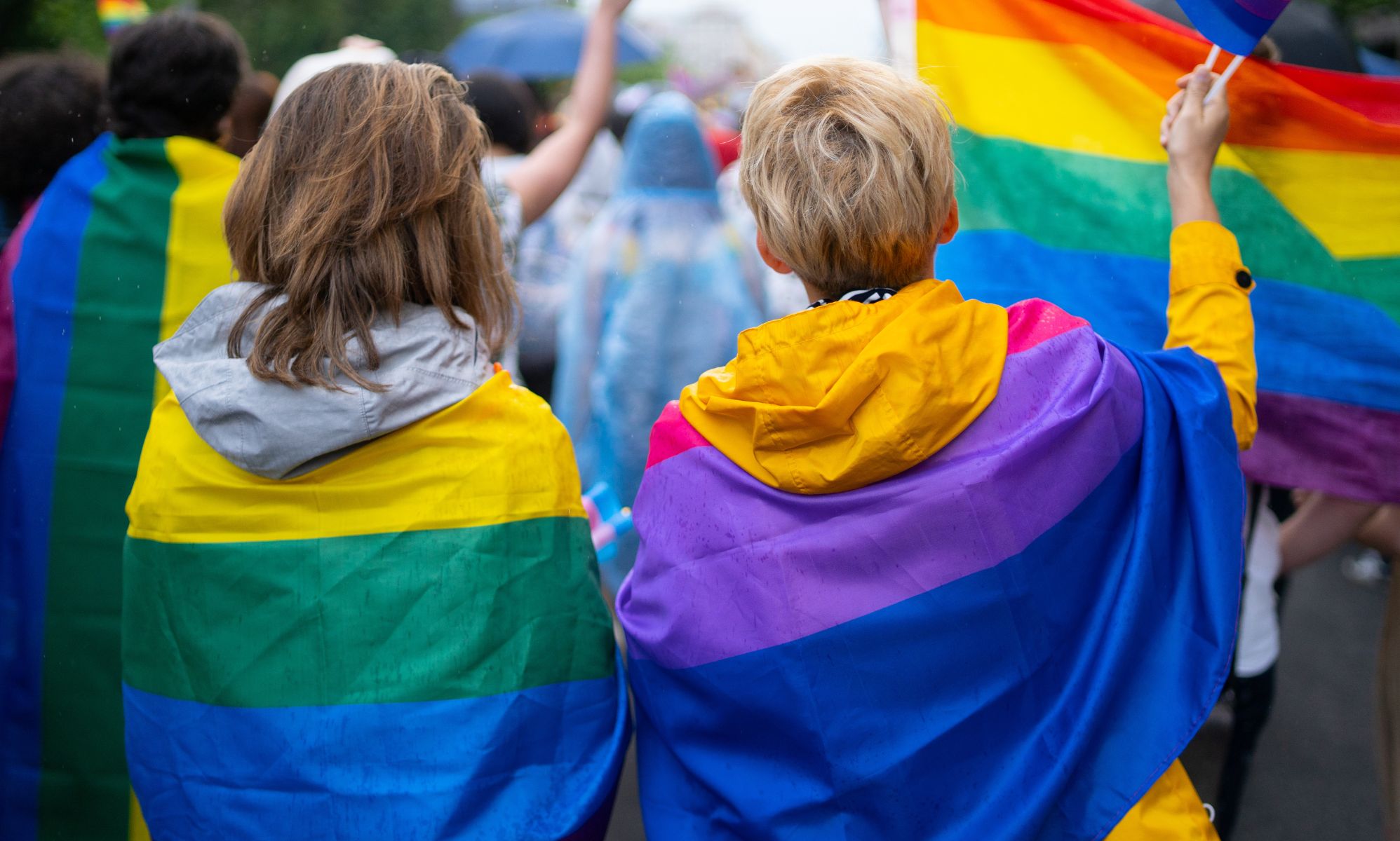 Two people with LGBTQ+ flags over their shoulders.