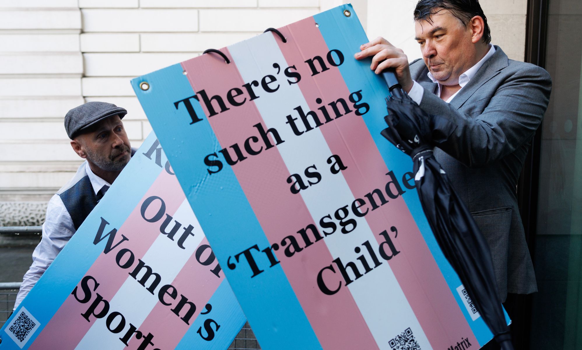 Graham Linehan putting on a wooden placard outside the courthouse. 