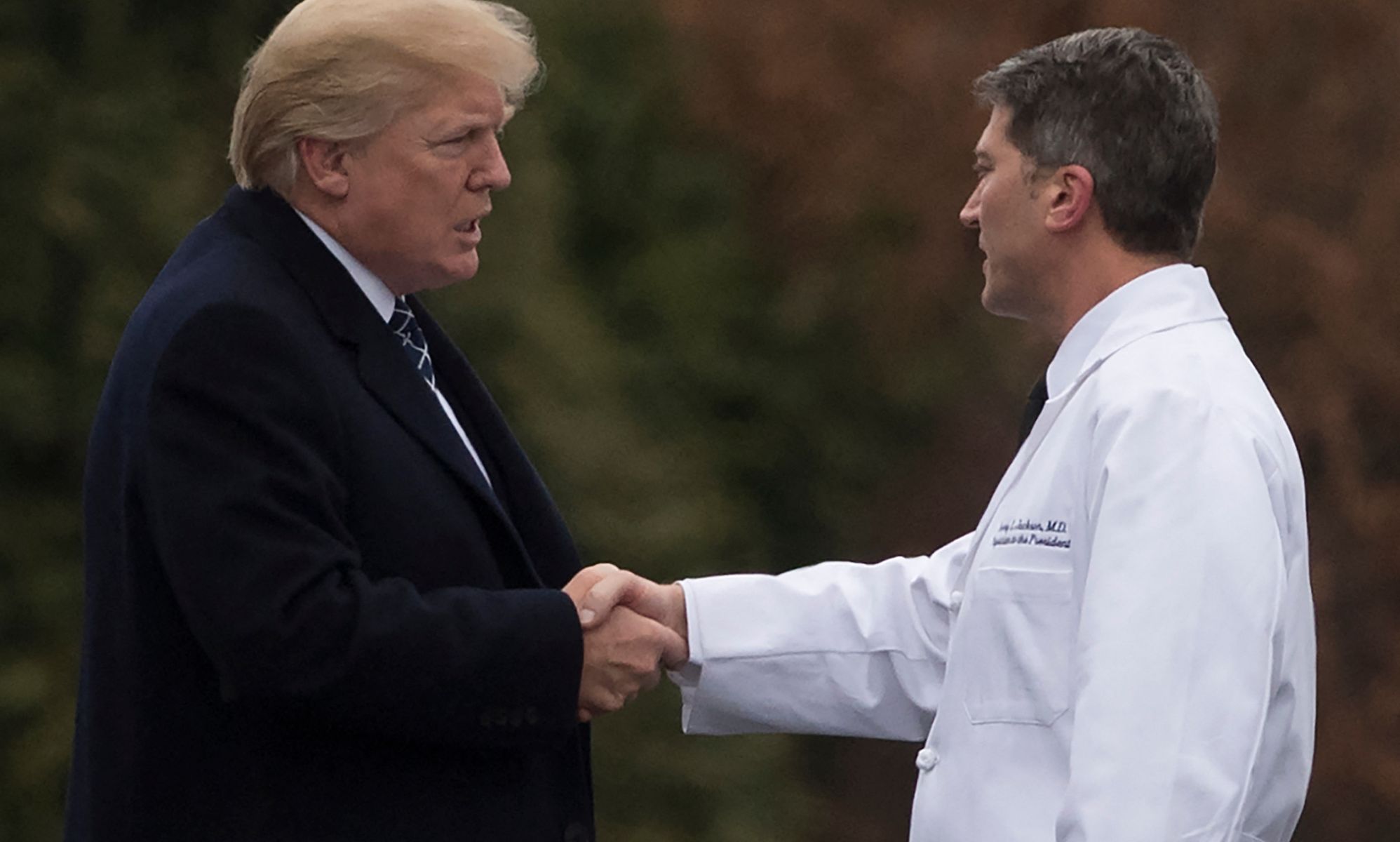 Ronny Jackson, on the right, shaking hands with Donald Trump, left, outside in a field.