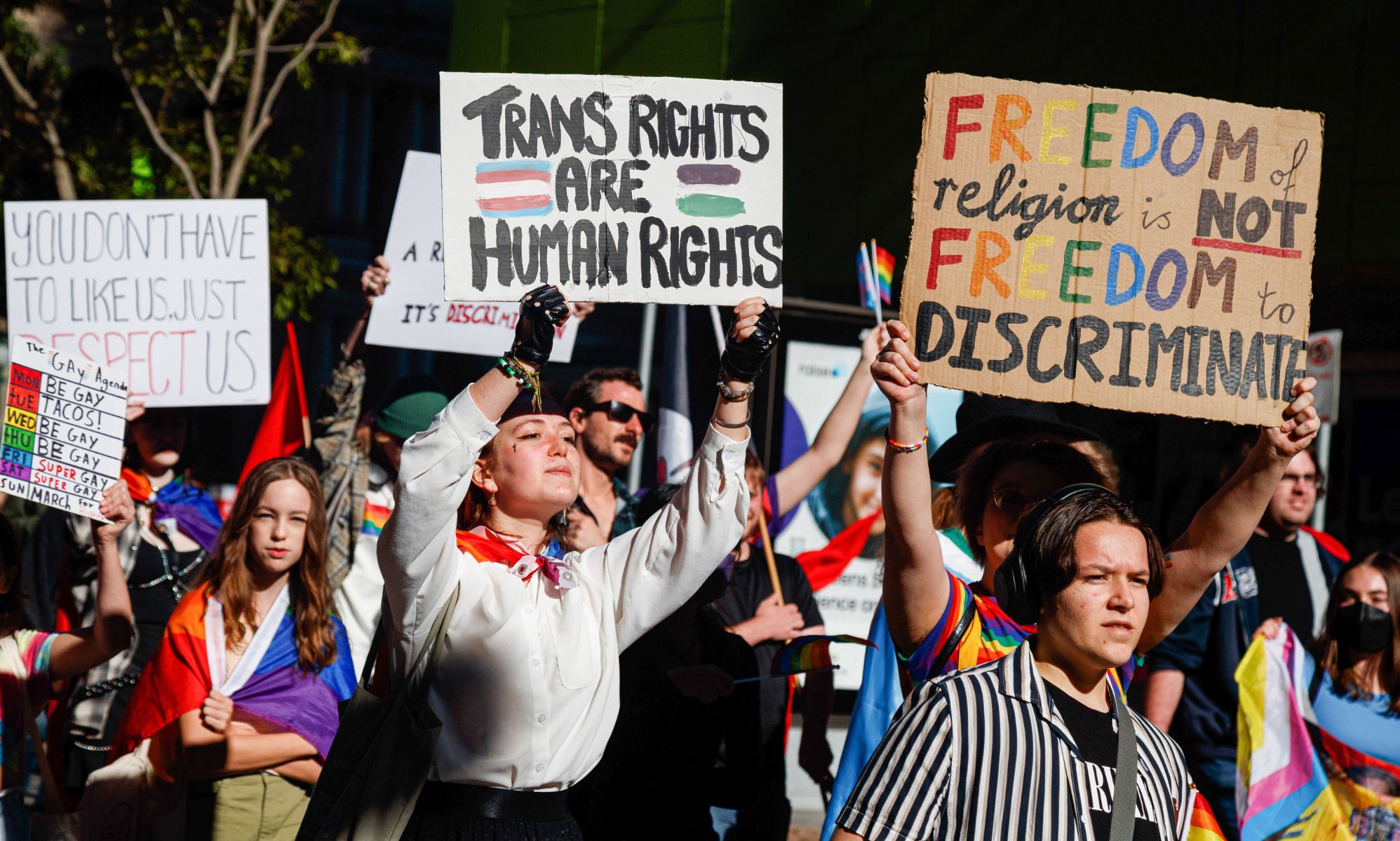 Protestors in Australia holding signs promoting LGBTQ+ rights.