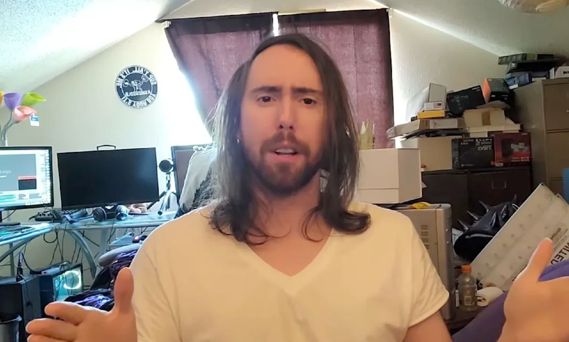 A picture of Asmongold speaking to a webcam inside his messy, messy room.