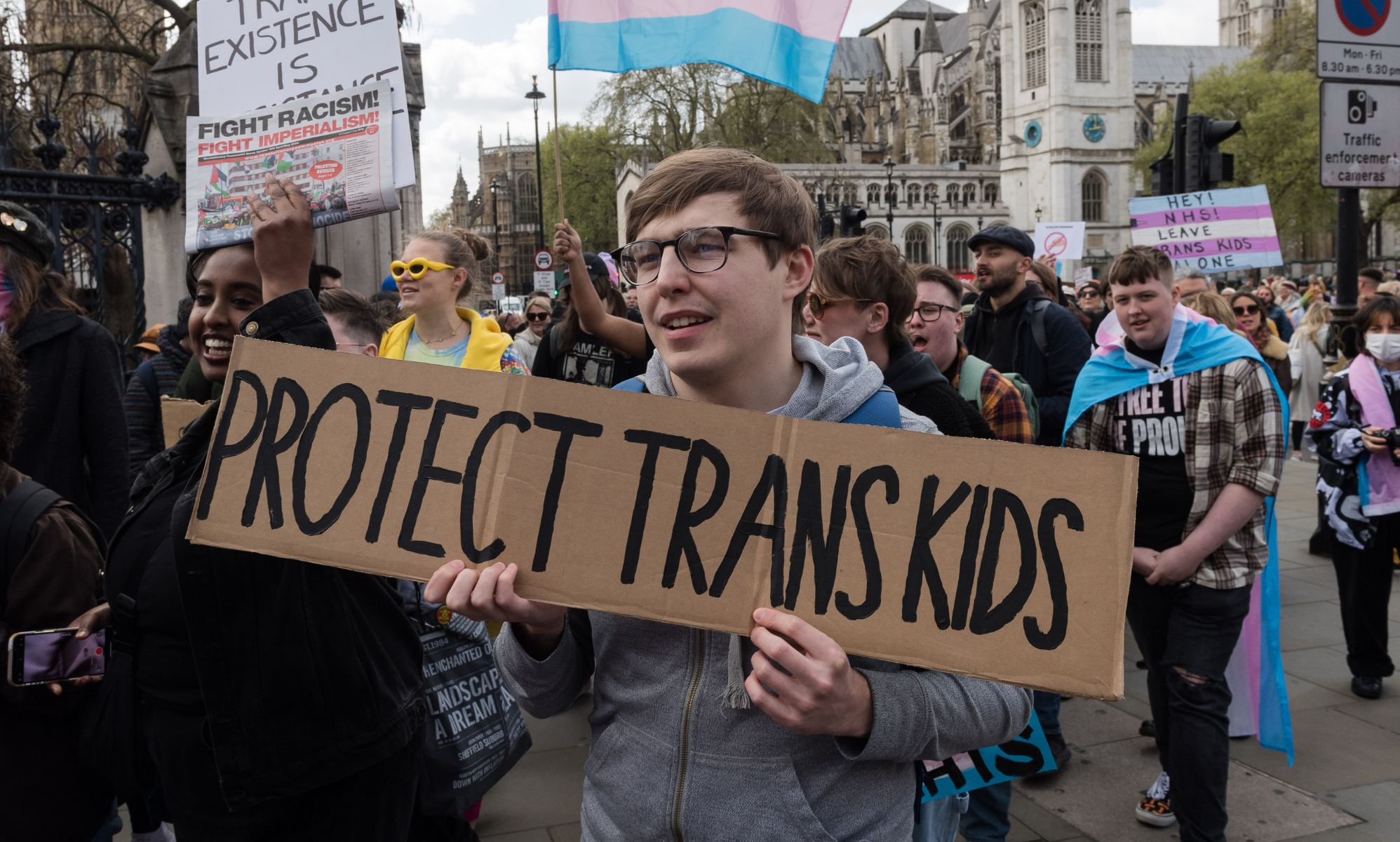 A person holding a sign reading &quot;protect trans kids&quot;