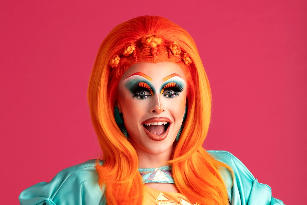 Blu Hydrangea with a bright orange wig and blue dress against a pink background.