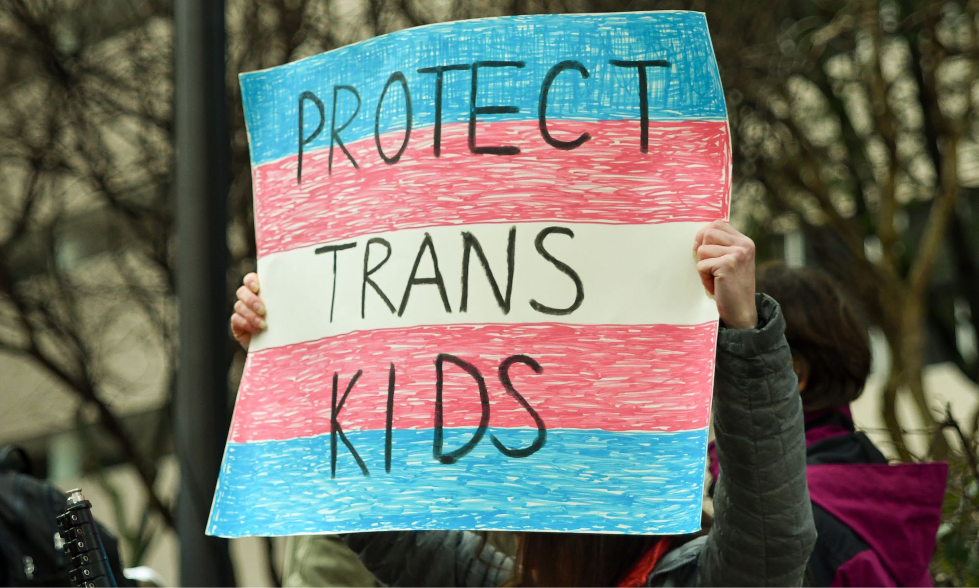 A protestor holds up a sign reading “Protect Trans Kids.”