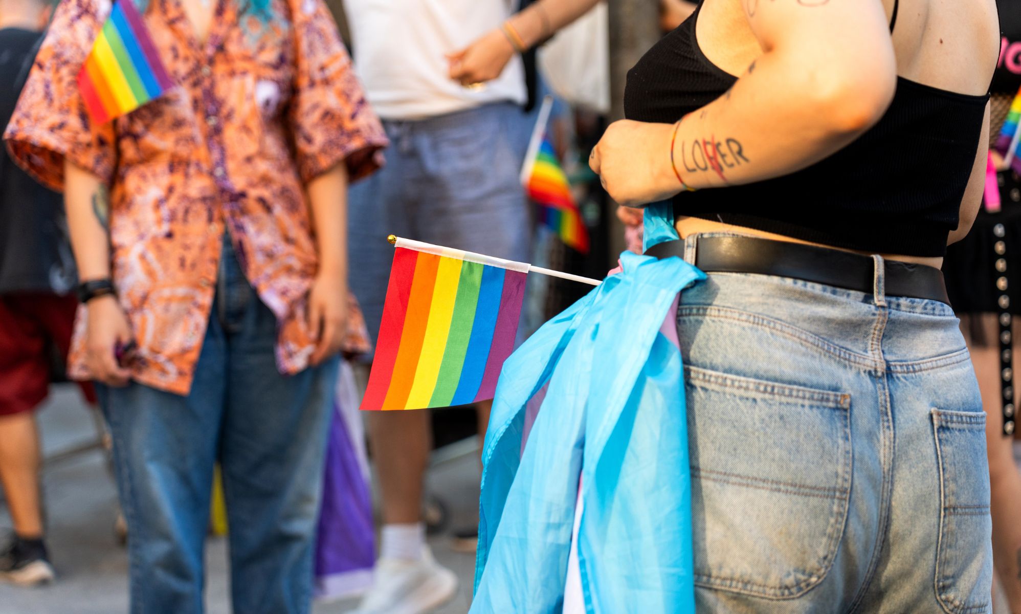 An anonymous person tying a trans flag to their belt during a Pride protest.