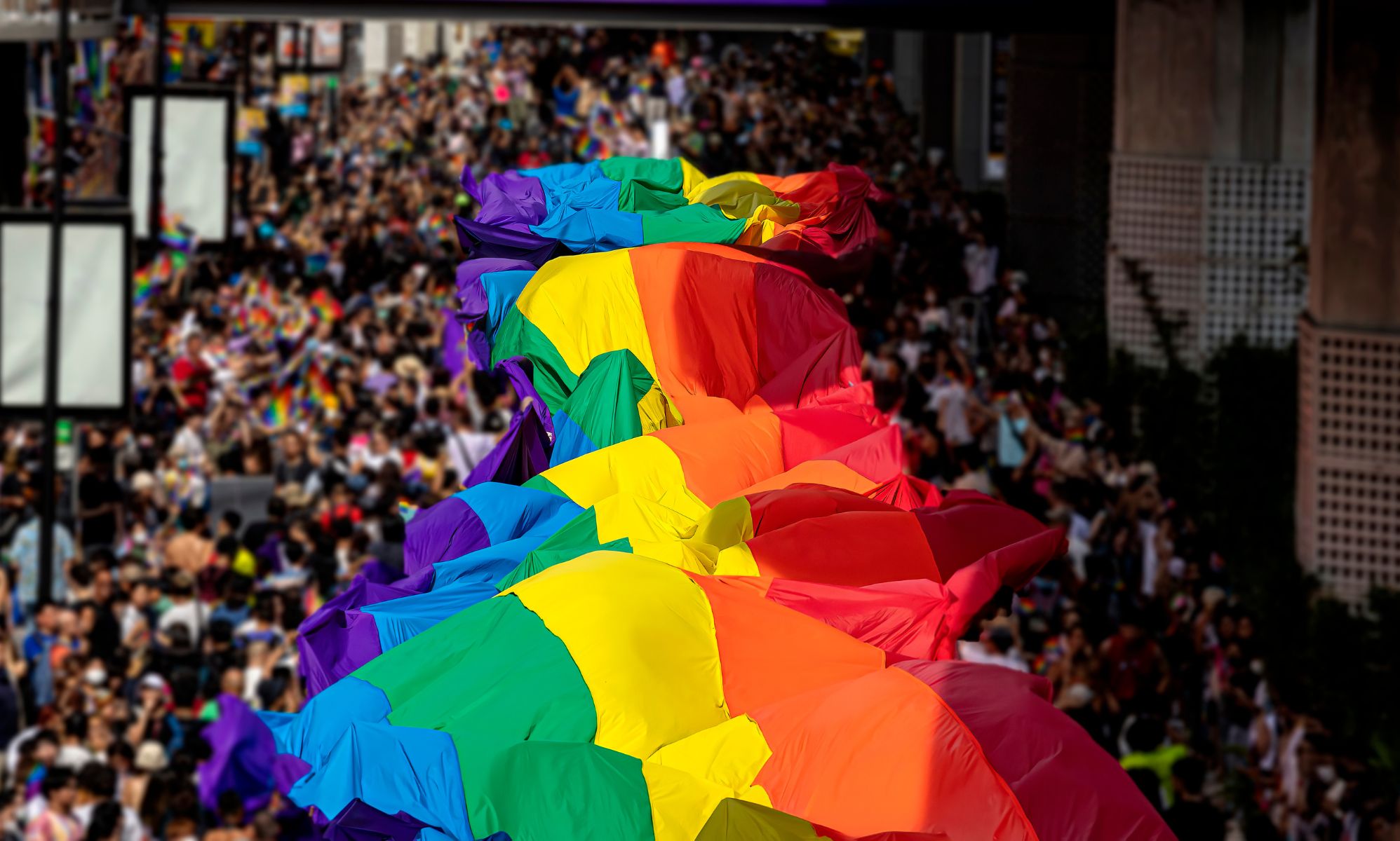 A huge LGBTQ+ Pride banner across a crowd of people.