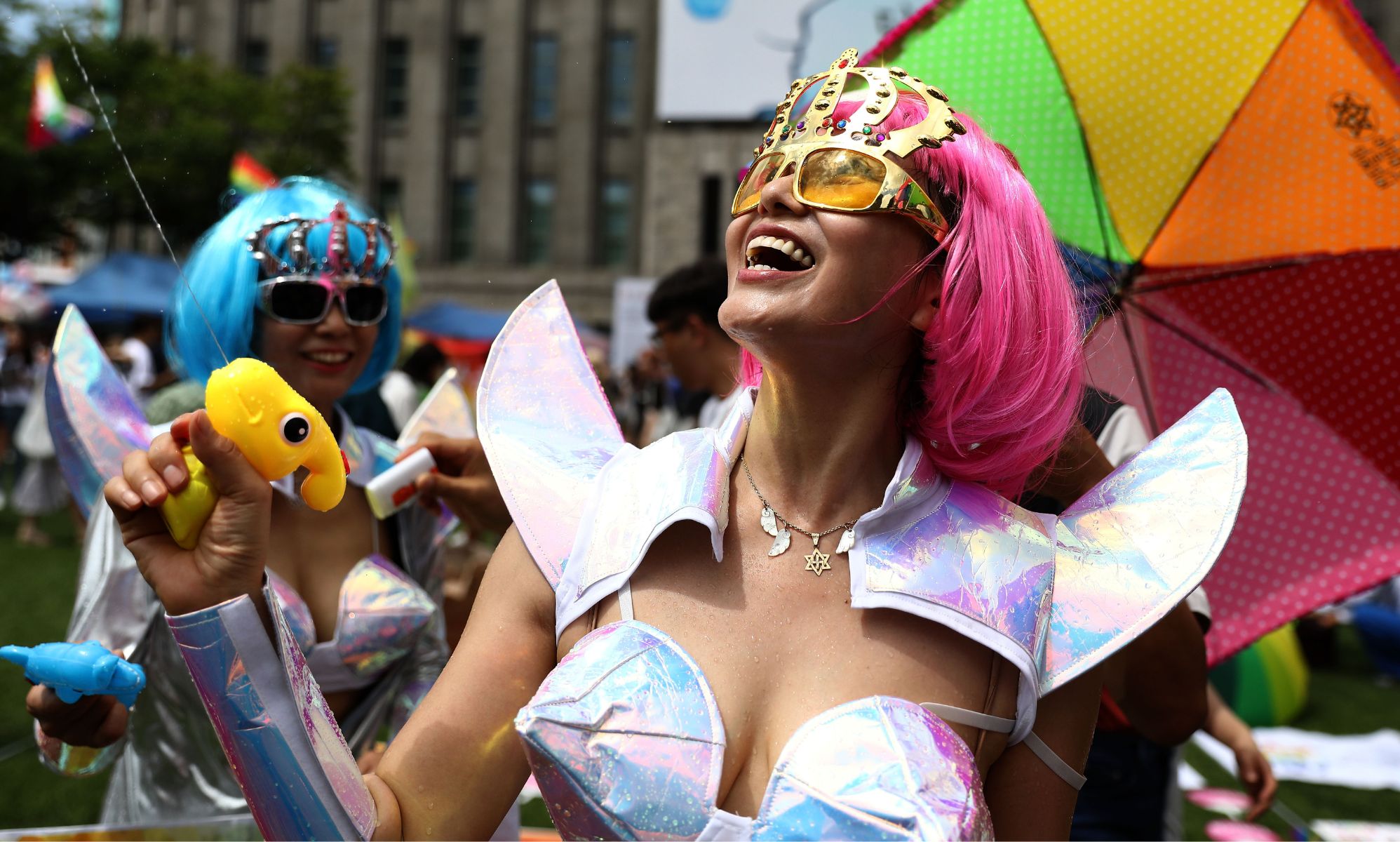 A person in a Pride outfit using a water pistol.